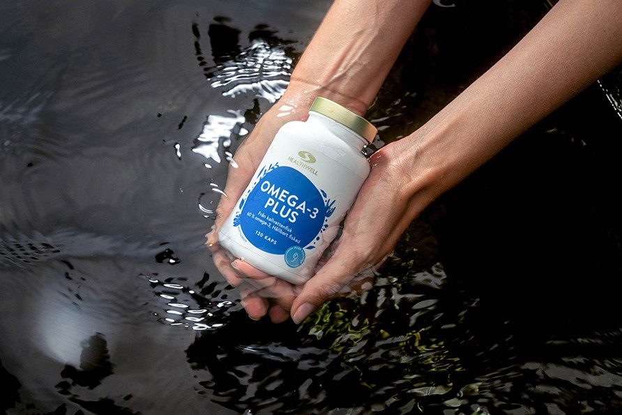 Tv� h�nder h�ller en burk Healthwell Omega-3 Plus ovanf�r m�rkt, krusigt vatten.