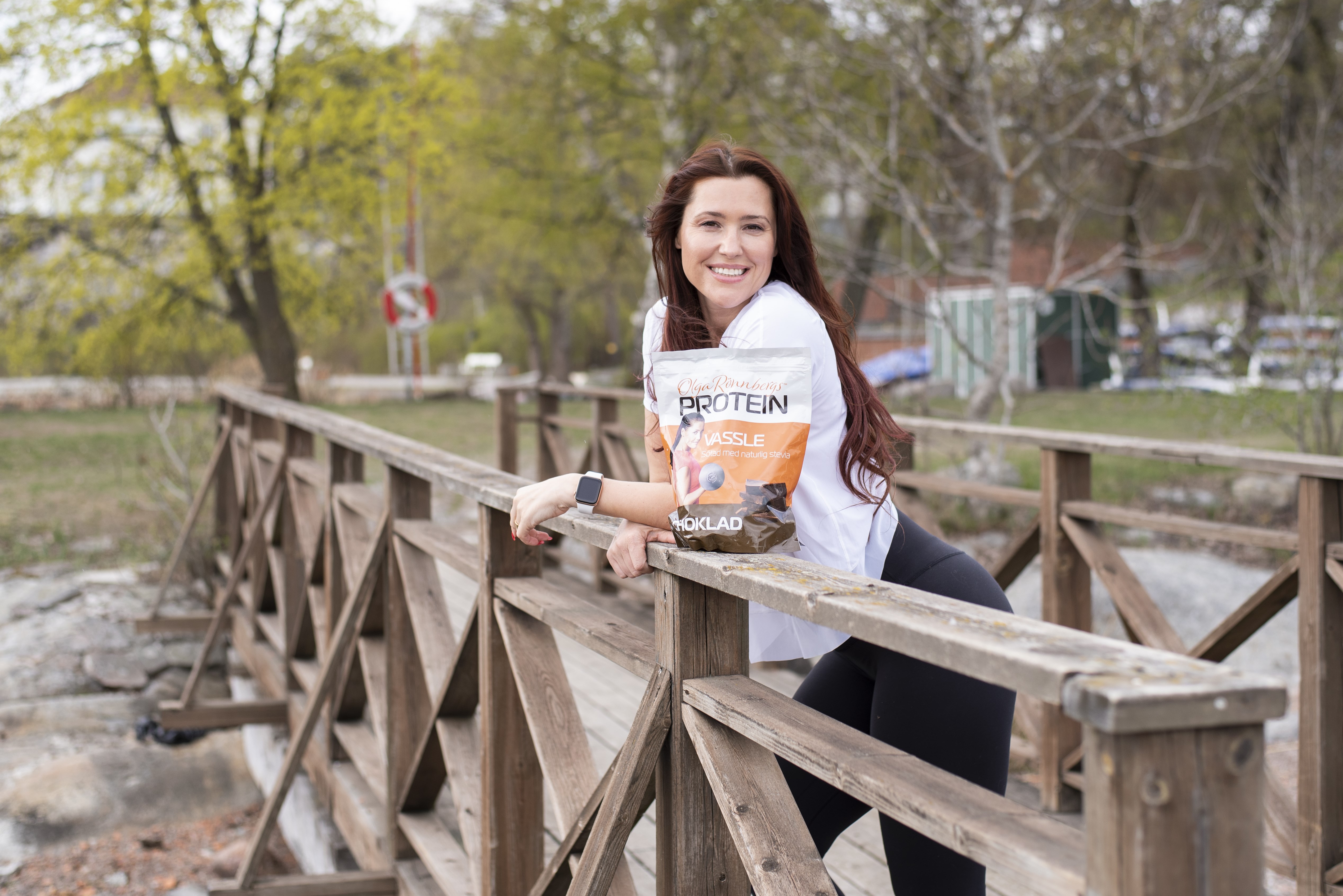 Olga Rönnberg lutar sig glatt mot ett broräcke med en påse av sitt eget protein framför sig. Olga Rönnberg lutar sig glatt mot ett broräcke med en påse av sitt eget protein framför sig.