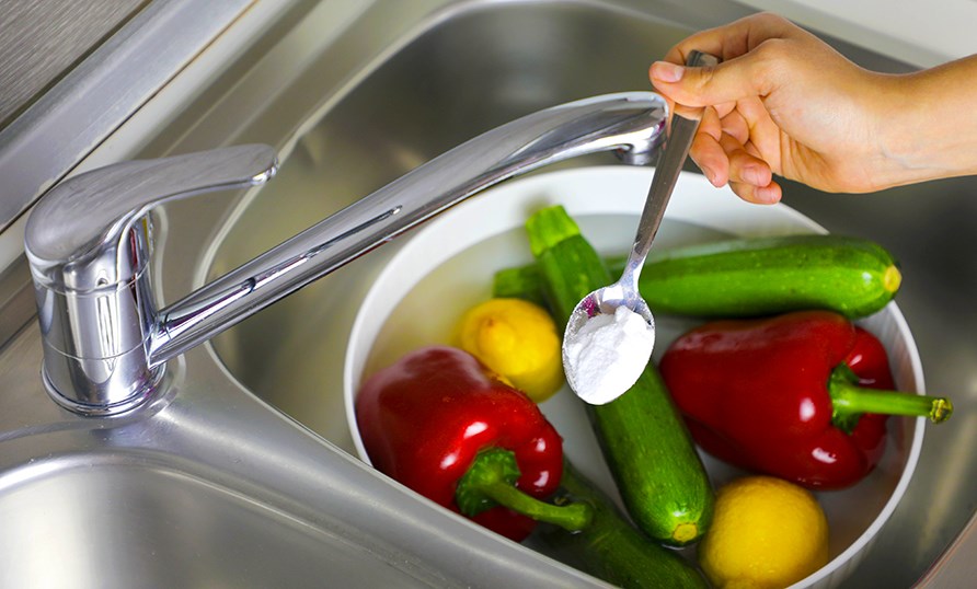 En skl med grnsaker och en hand som hller i en tsk med bikarbonat. 