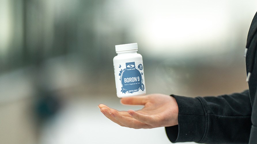 Bilden visar en hand som kastar upp produkten Healthwell Boron 9 i luften. Bakgrunden r suddig. 