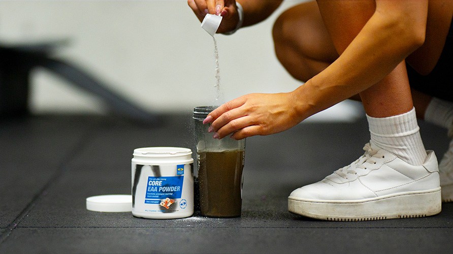 En person hller en skopa Core EAA Powder i en shaker.