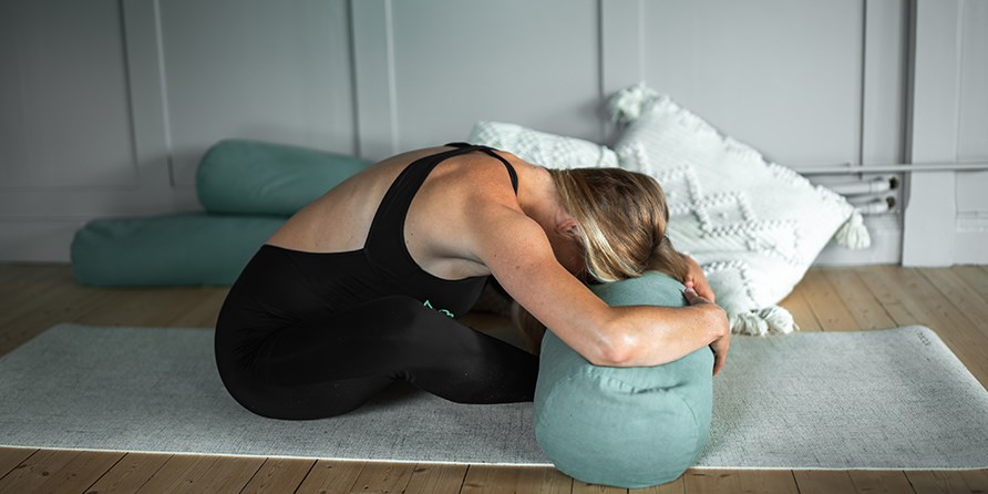 Kvinna med träningskläder som befinner sig i ett rum sittandes i en stretchande ställning med huvudet rikat mot en yogamatta som hon sitter på. Kvinna med träningskläder som befinner sig i ett rum sittandes i en stretchande ställning med huvudet rikat mot en yogamatta som hon sitter på.