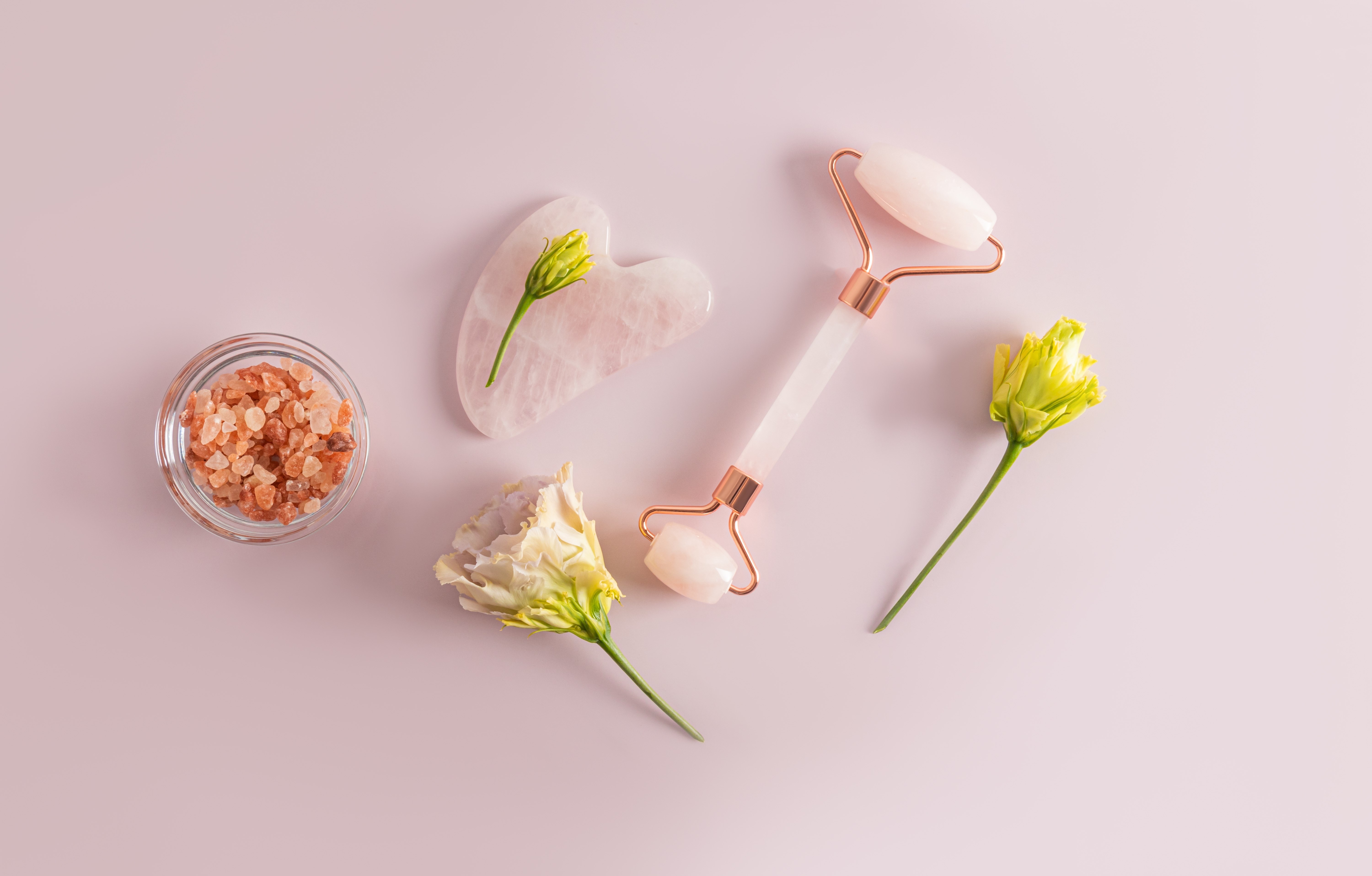 Gua sha-verktyg i rosa f�rg tillsammans med torkade blommor och sten i en liten sk�l.