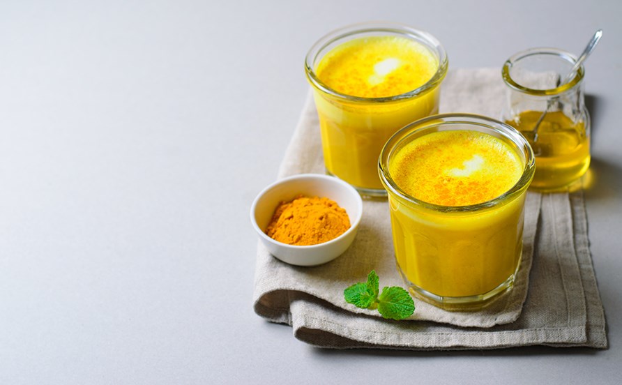 Glas med guldmjlk, flytande honung och en skl med gurkmejapulver.