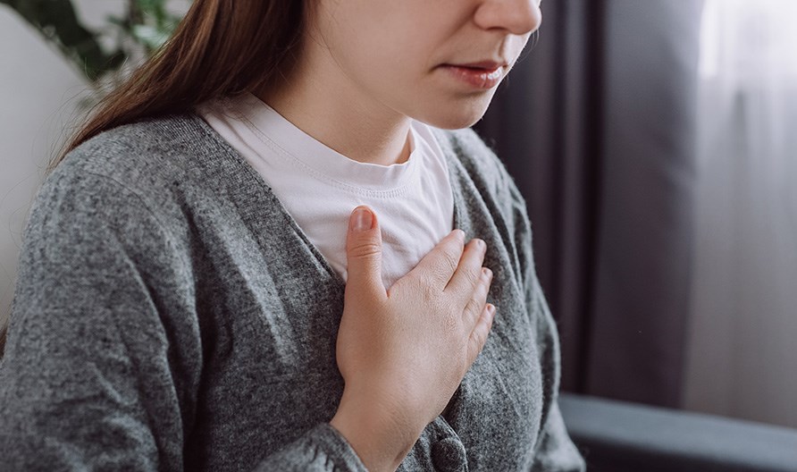 Kvinna som har sin ena hand p� br�stkorgen.