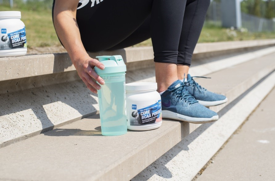 Halvbild p en person som sitter i en trappa med en shaker och en burk BCAA bredvid sig.