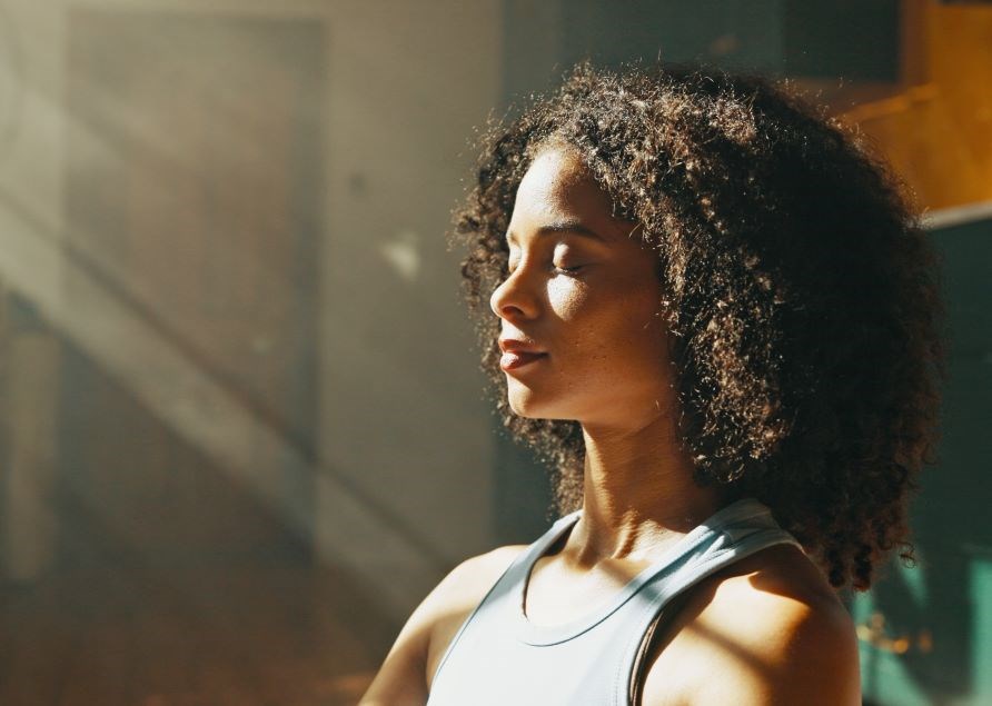 Kvinna njuter av solstrlar som lyser in genom fnstret.