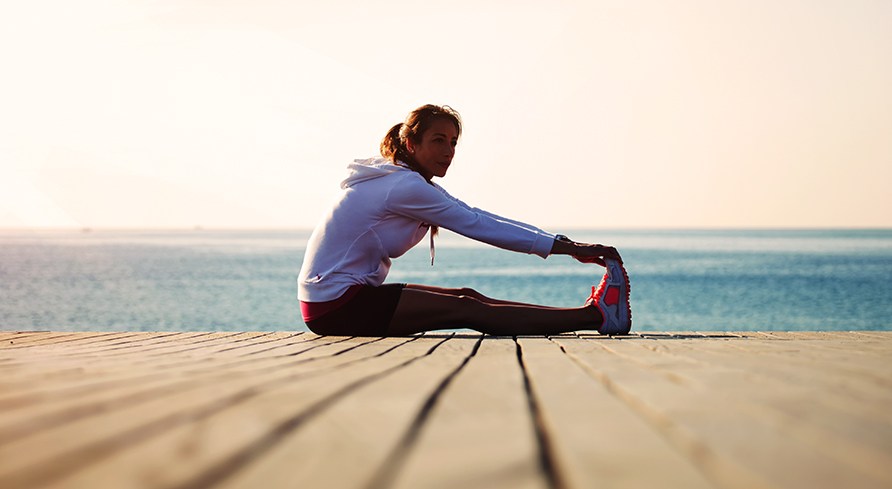 En tjej sitter p� en brygga och stretchar.