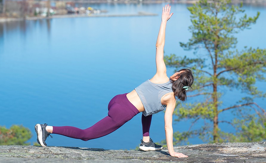 En kvinna som stretchar p� en klippa vid havet