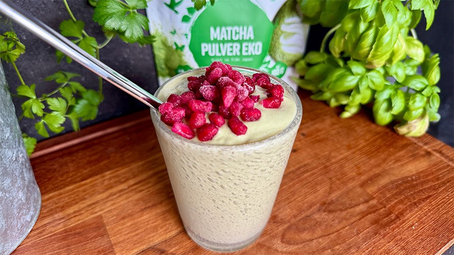 Healthwell Matcha Pulver EKO i originalf�rpackning, Kalorismarts matchasmoothie i ett glas toppad med b�r, kruka och basilika p� ett tr�bord. 