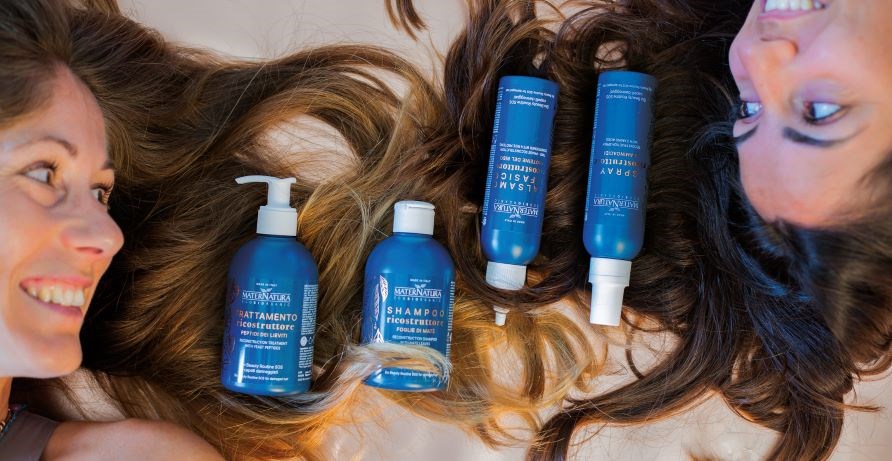 Tv� leende kvinnor som ligger ned och tittar p� varandra med sitt h�r utspritt mellan sig. P� h�ret vilar flaskor med h�rv�rdsprodukter. 