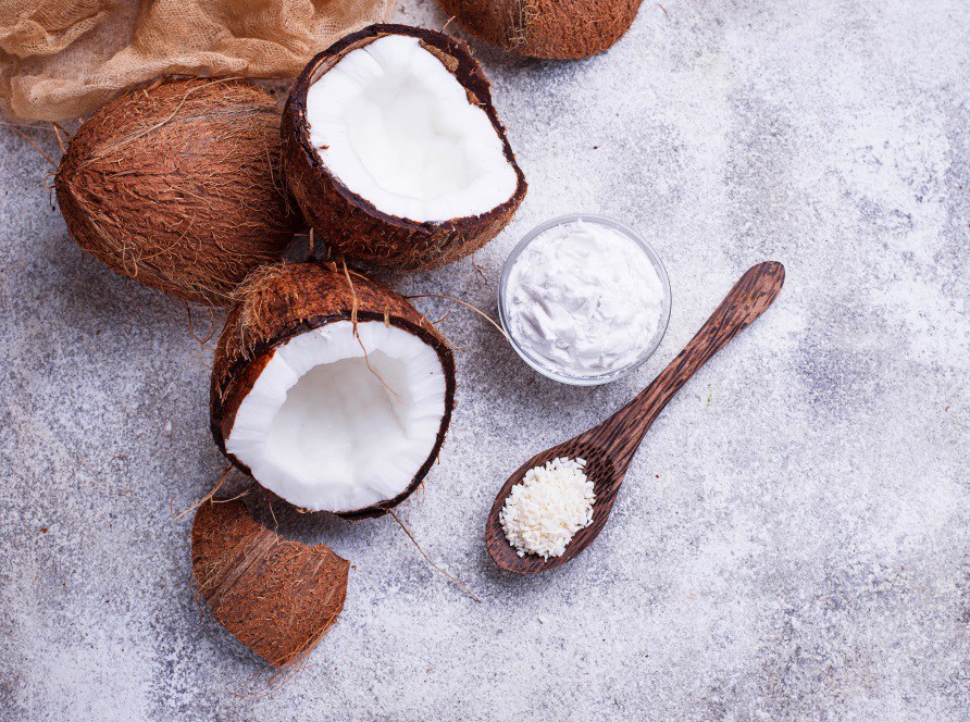 Kokosntter, en skl med kokosolja och kokosflingor p en gr stenyta.