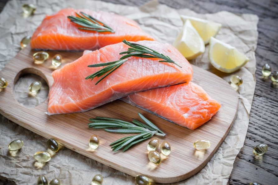 Tre laxfiler p en skrbrda tillsammans med omega-3-kapslar och citronklyftor. 
