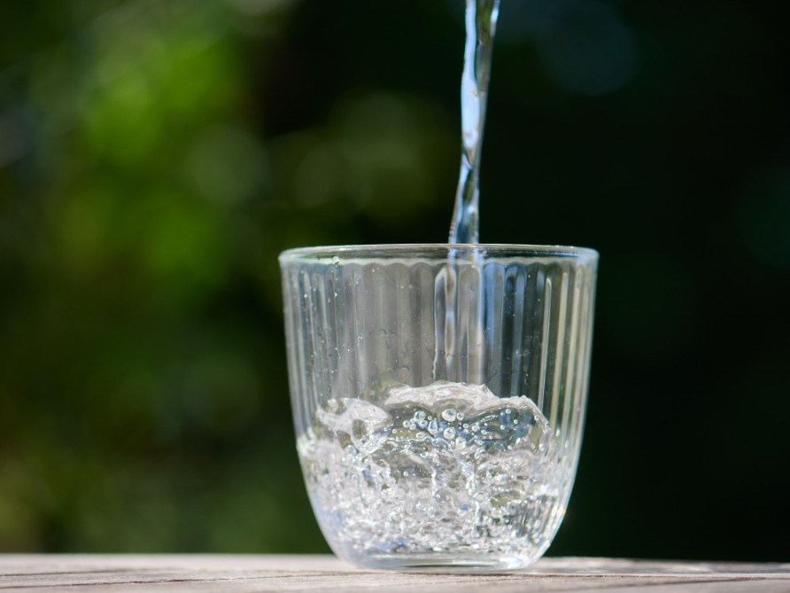 Ett glas vatten som fylls p� mot en gr�n bakgrund. 