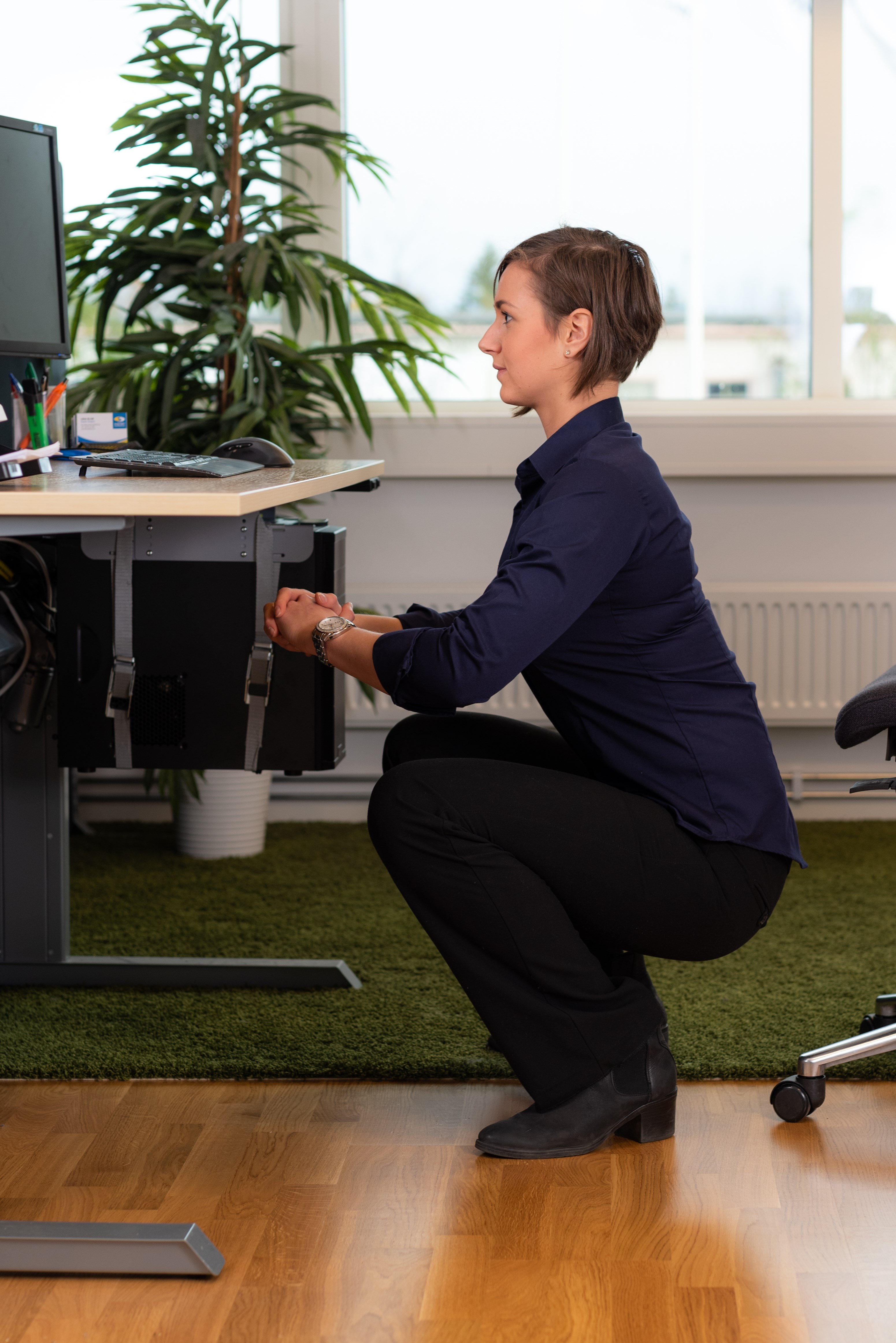 En kontorsklädd kvinna sitter på huk med rak rygg framför sitt skrivbord. En kontorsklädd kvinna sitter på huk med rak rygg framför sitt skrivbord.