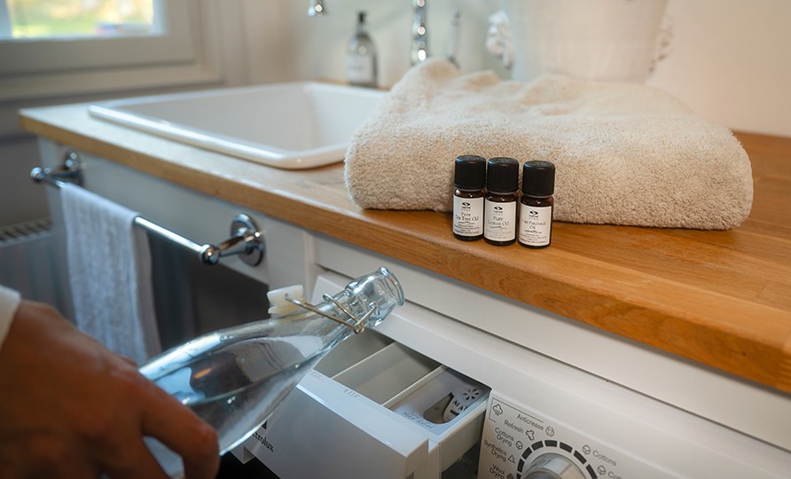 Kvinna som hller egengjort skljmedel ur en glasflaska ner i skljmedelsfacket p tvttmaskinen.