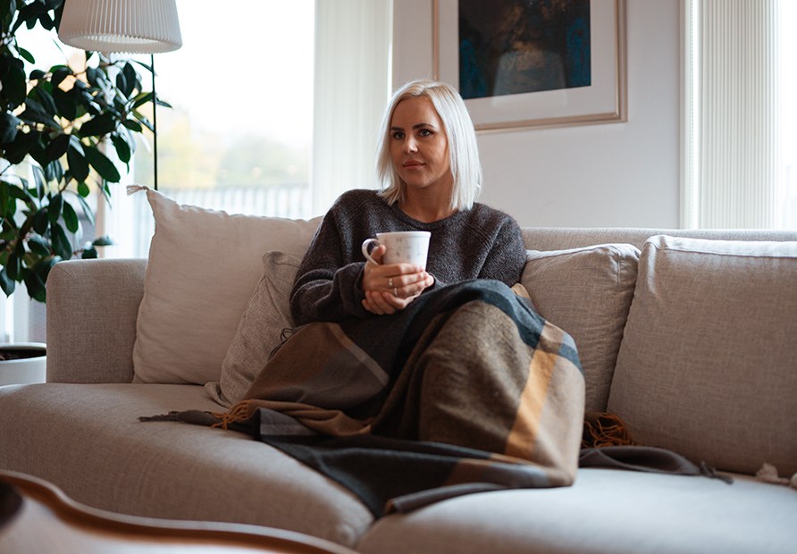 Hlsocoach Susanna Jungblom sitter uppkrupen i en soffa med en filt och en kopp te.