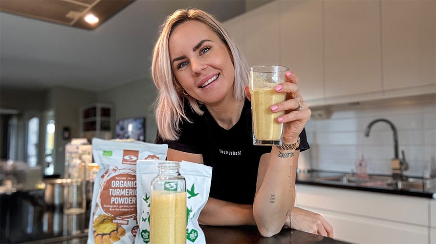 Susanna Jungblom ler stort och lutar sig mot en k�ksb�nk medan hon h�ller i ett glas Golden Glow Smoothie. 