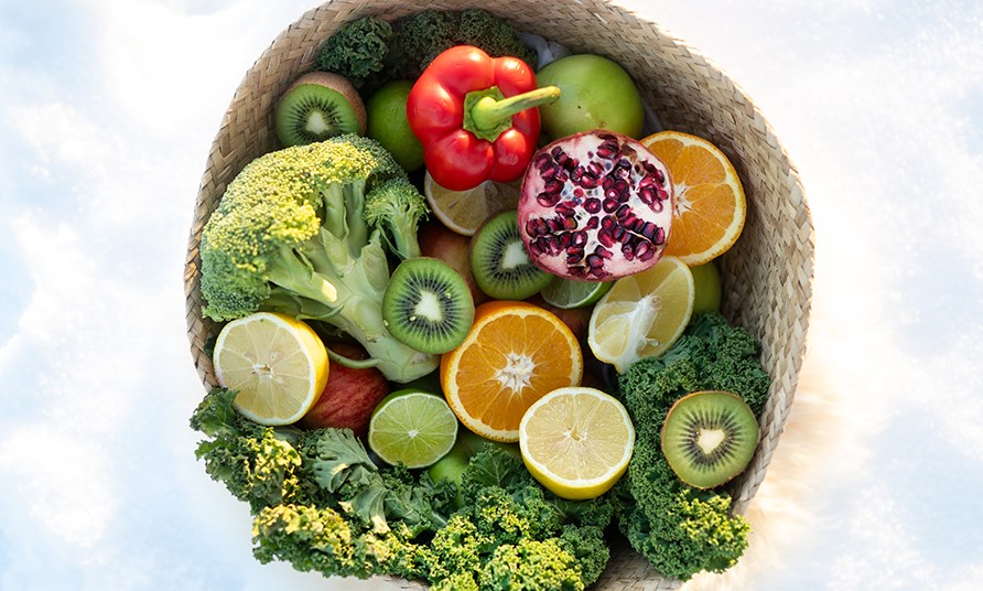 Nrbild p frgglada grnsaker och frukter i en fltad korg.